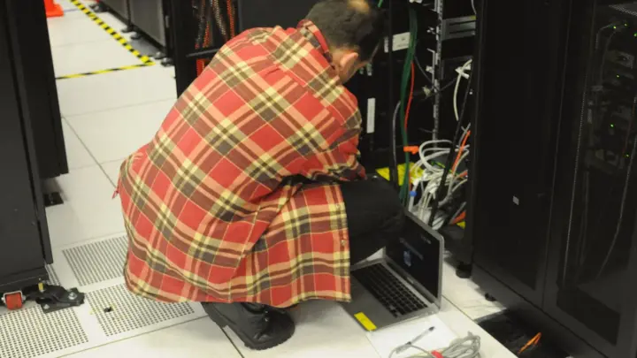 A technician with a laptop working at a server rack