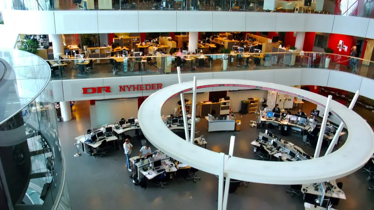 A busy television newsroom with rows of desks and screens