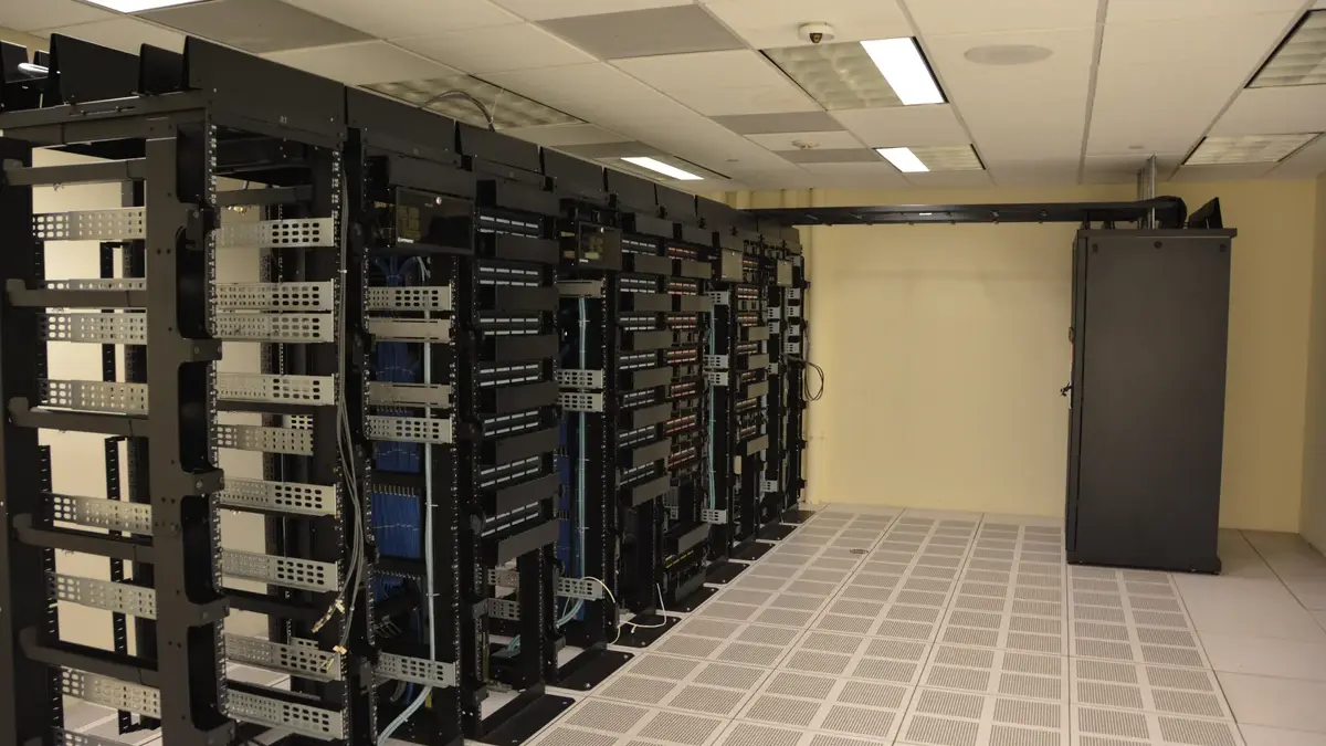 Rows of black server racks with network cabling in a data centre with a white raised floor
