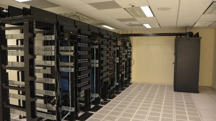 Rows of black server racks with network cabling in a data centre with a white raised floor