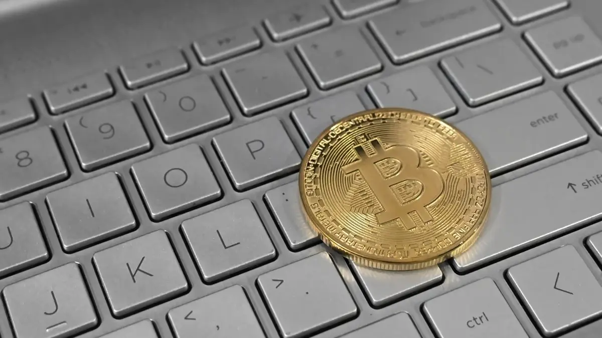A gold-coloured Bitcoin token resting on the keys of a silver laptop keyboard