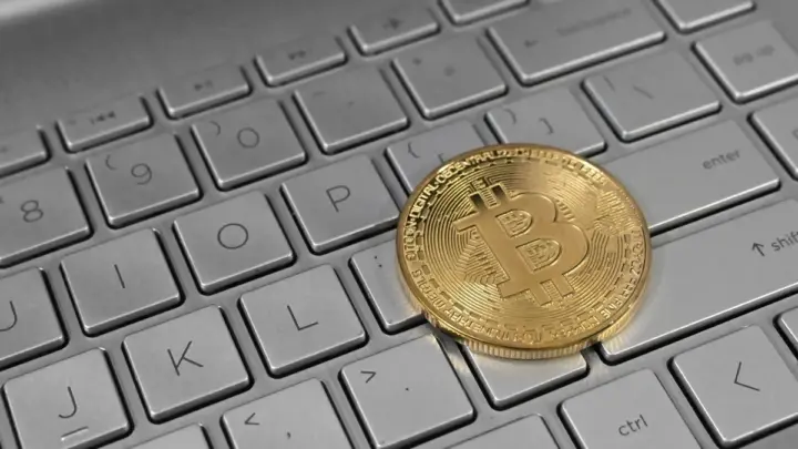 A gold-coloured Bitcoin token resting on the keys of a silver laptop keyboard
